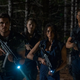 Characters from Resident Evil: Welcome to Raccoon City, aiming their guns down and standing in the woods at night.